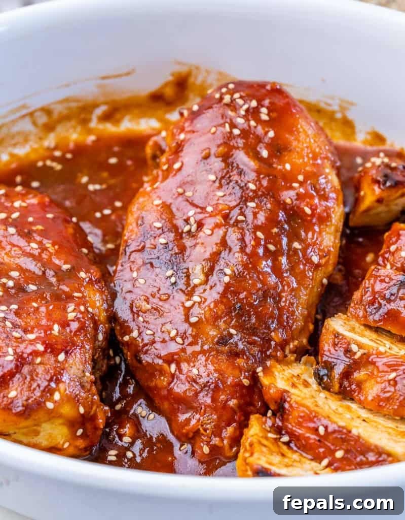 Sticky Honey Sriracha Chicken 8 Side shot of chicken breast in a dish coated with an orange sauce, freshly baked and glistening.