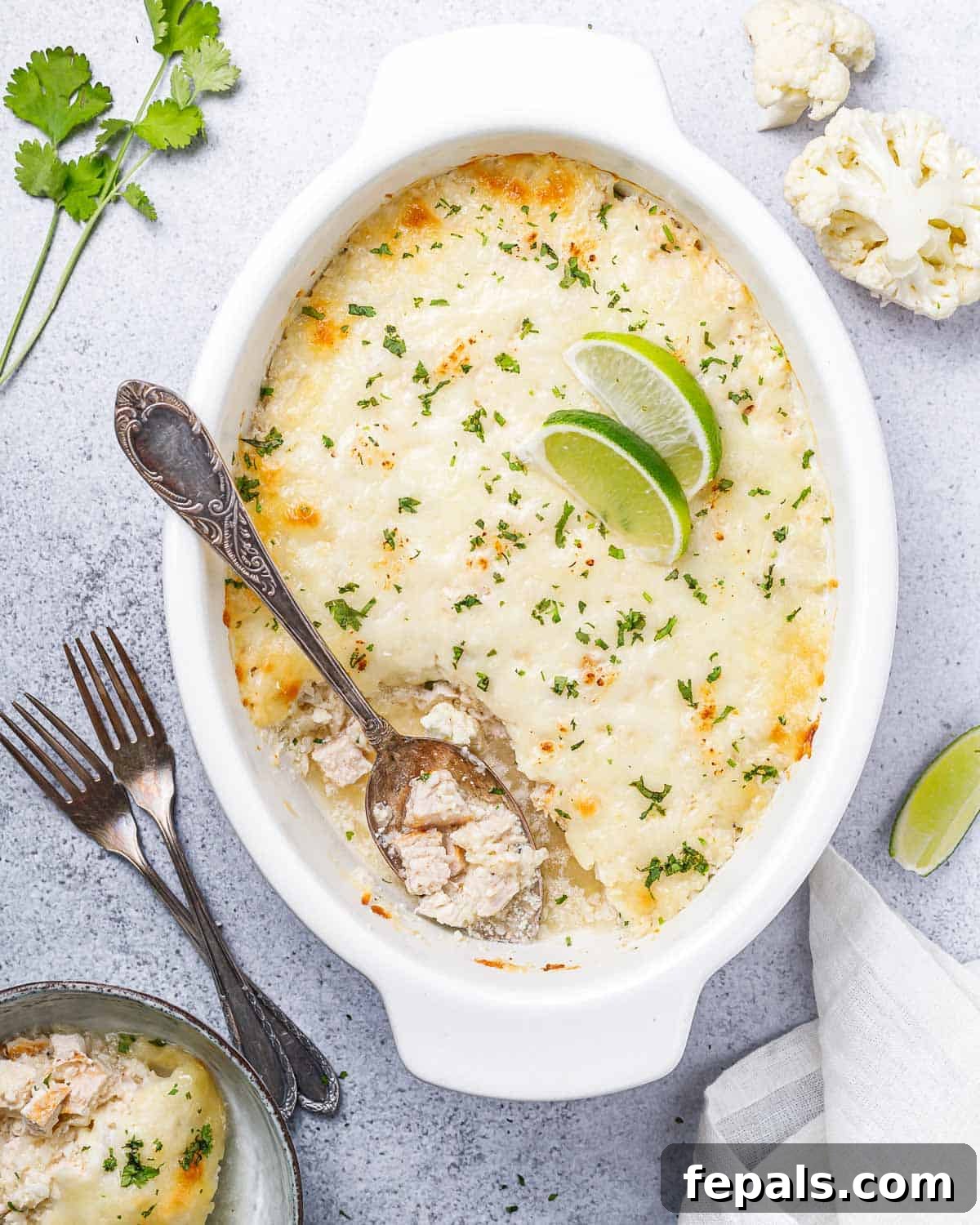 A spoon scooping a portion of chicken and cauliflower rice casserole from a white baking dish, showing the depth and texture of the dish.