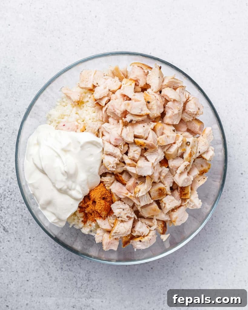 A close-up view of chopped chicken being mixed with sour cream and taco seasoning in a bowl, illustrating the creamy coating process.