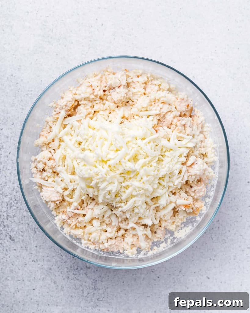 Shredded cheese being added to the chicken and cauliflower rice mixture in a bowl, ready to be folded in.