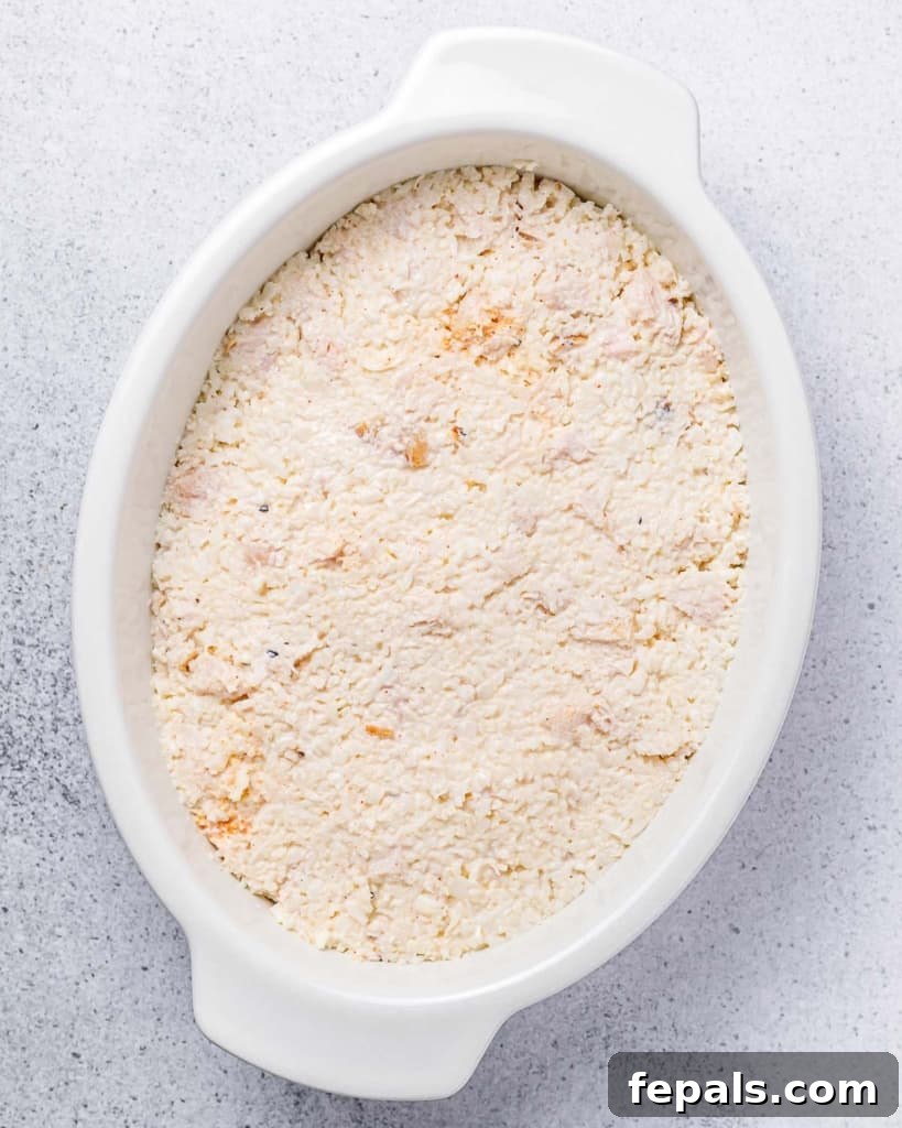 The chicken and cauliflower rice mixture neatly transferred into a white casserole dish, smoothed out with a spatula.