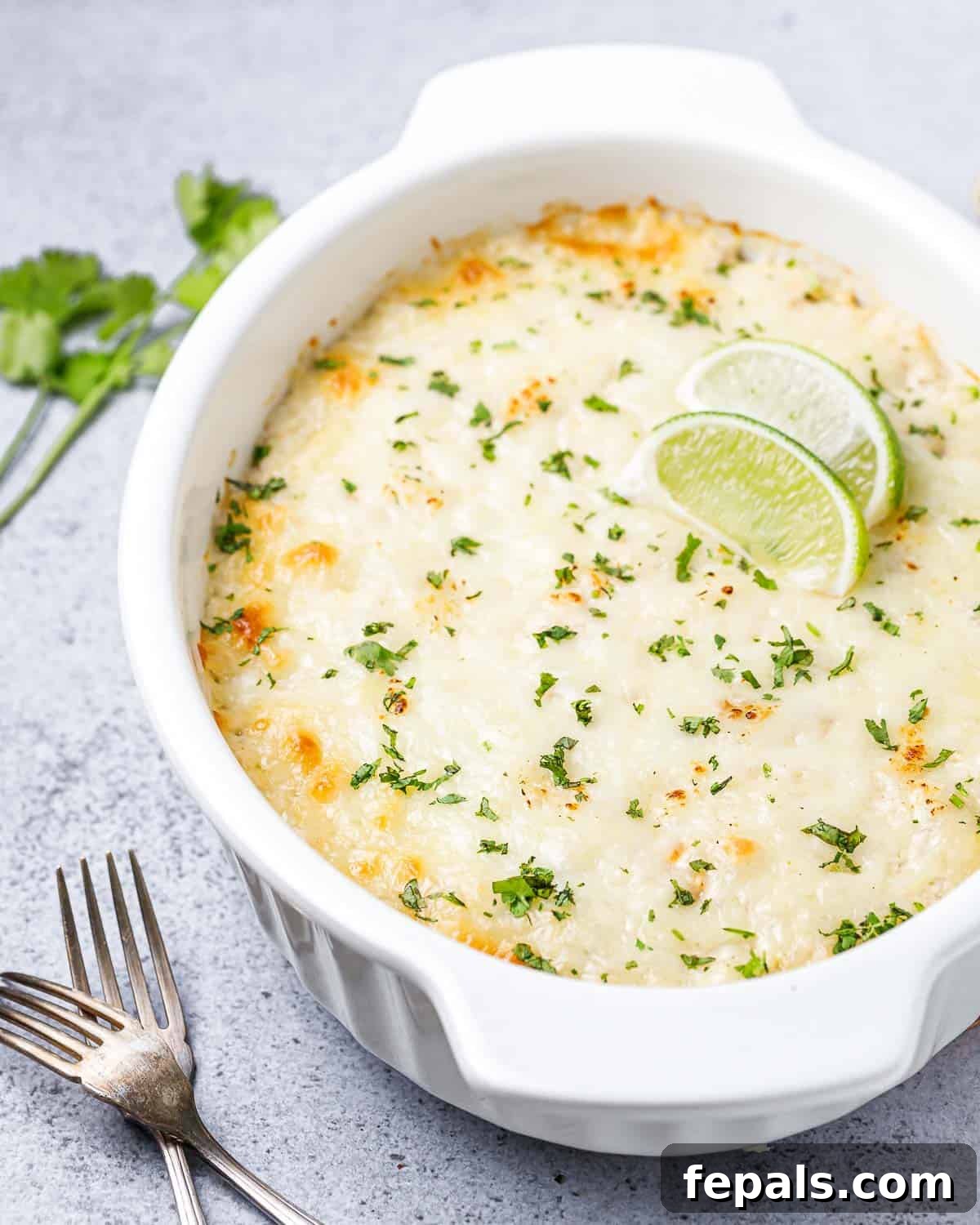 A freshly baked chicken and cauliflower rice casserole, garnished with bright green chopped cilantro and two lime wedges, ready for serving.