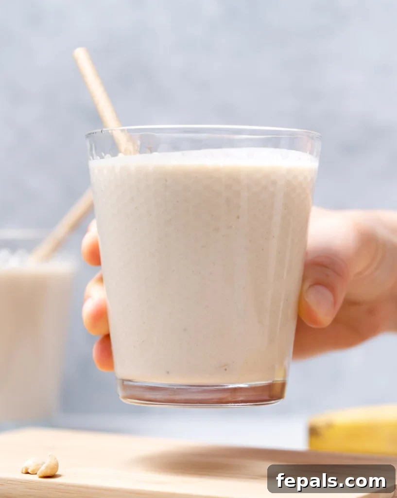 Nutty Banana Bliss Smoothie 12 Woman's hand holding a smoothie in a glass with a straw.
