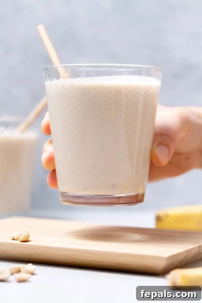 Nutty Banana Bliss Smoothie 9 Woman's hand holding a smoothie in a glass with a straw.