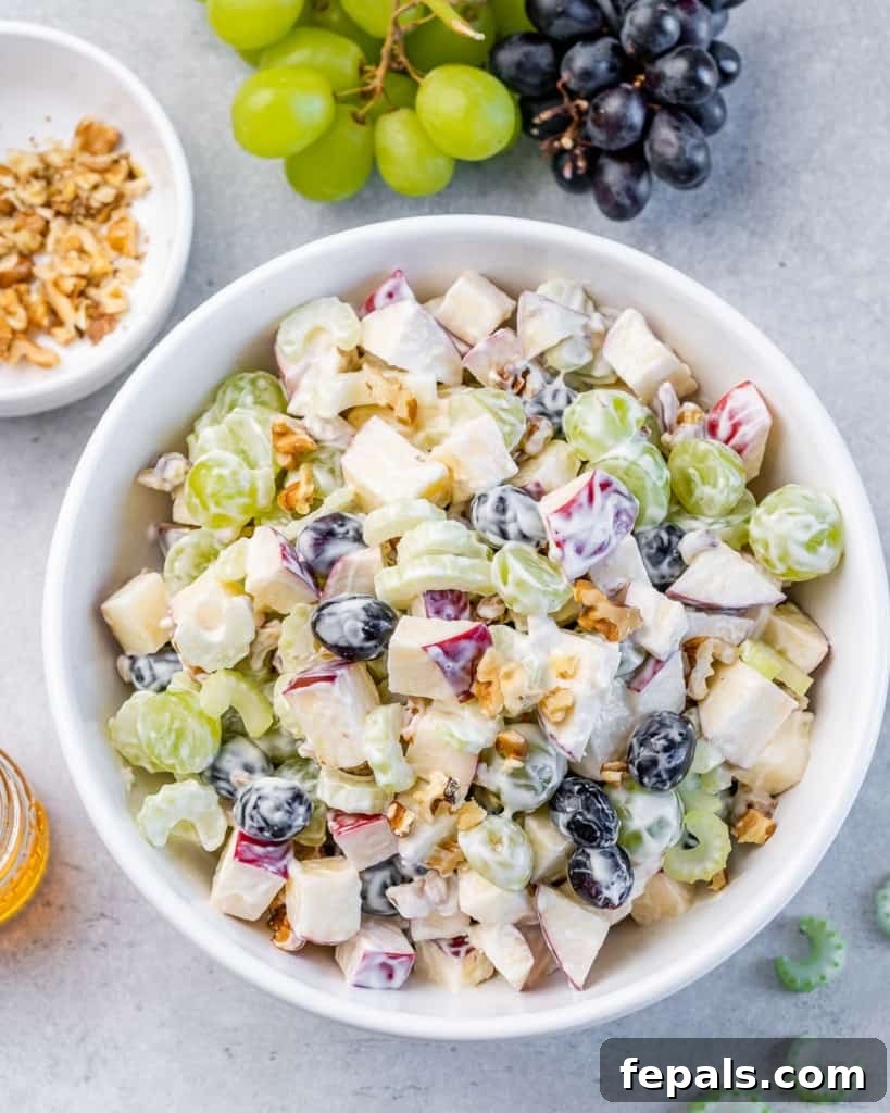 Top view of a creamy Waldorf Salad with apples, celery, grapes, and walnuts in a round bowl.