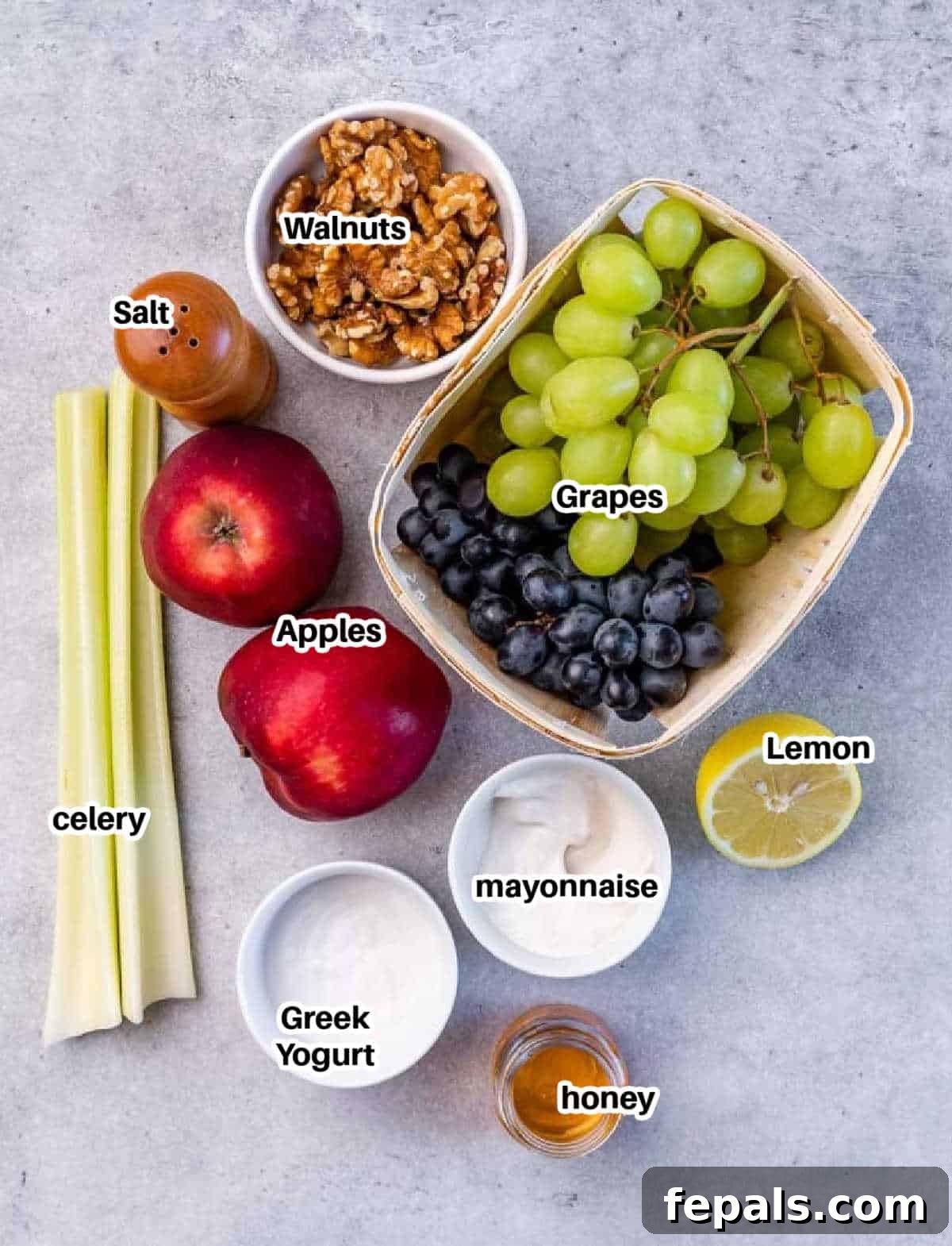 Ingredients for Waldorf salad including apples, celery, grapes, walnuts, yogurt, and mayonnaise laid out on a table.