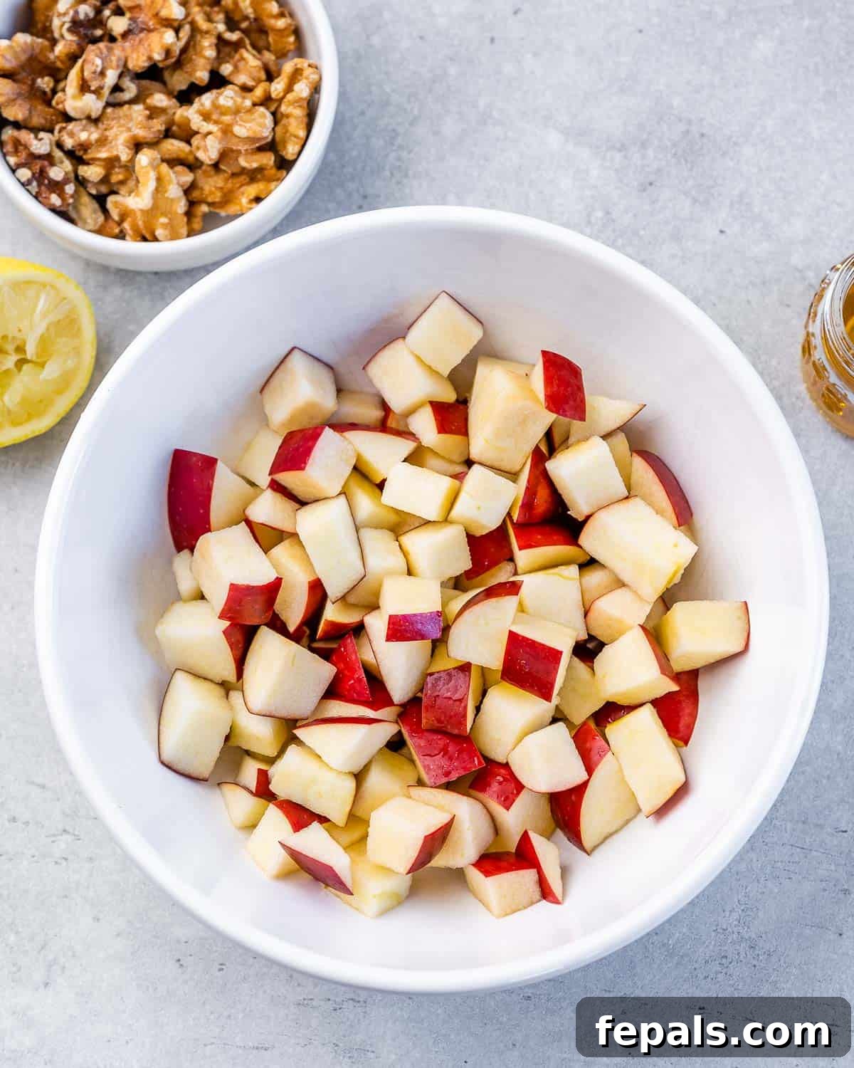 Diced apples in a white bowl, tossed with honey and lemon juice.