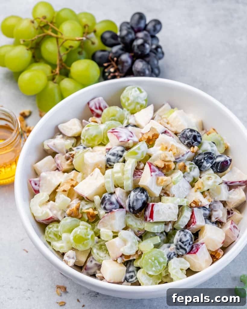 Waldorf Salad recipe in a white bowl, placed next to a bunch of fresh grapes.