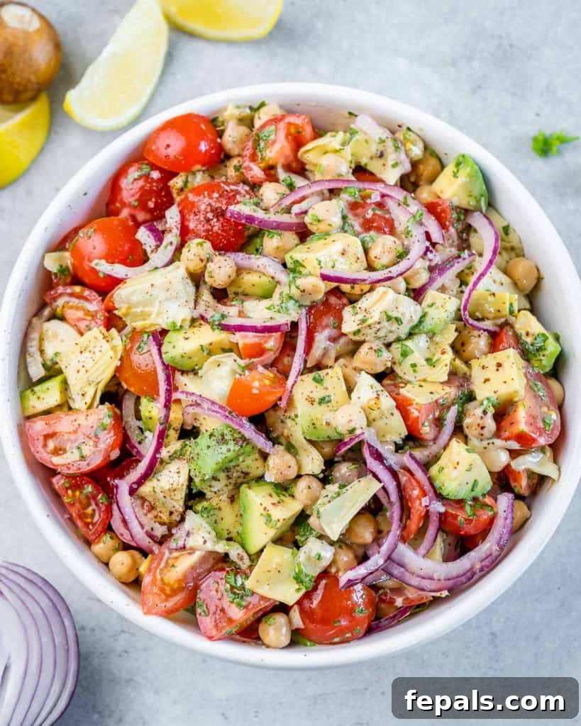 Top view of a vibrant Mediterranean Artichoke and Tomato Salad with chickpeas, red onion, and avocado in a round white bowl.