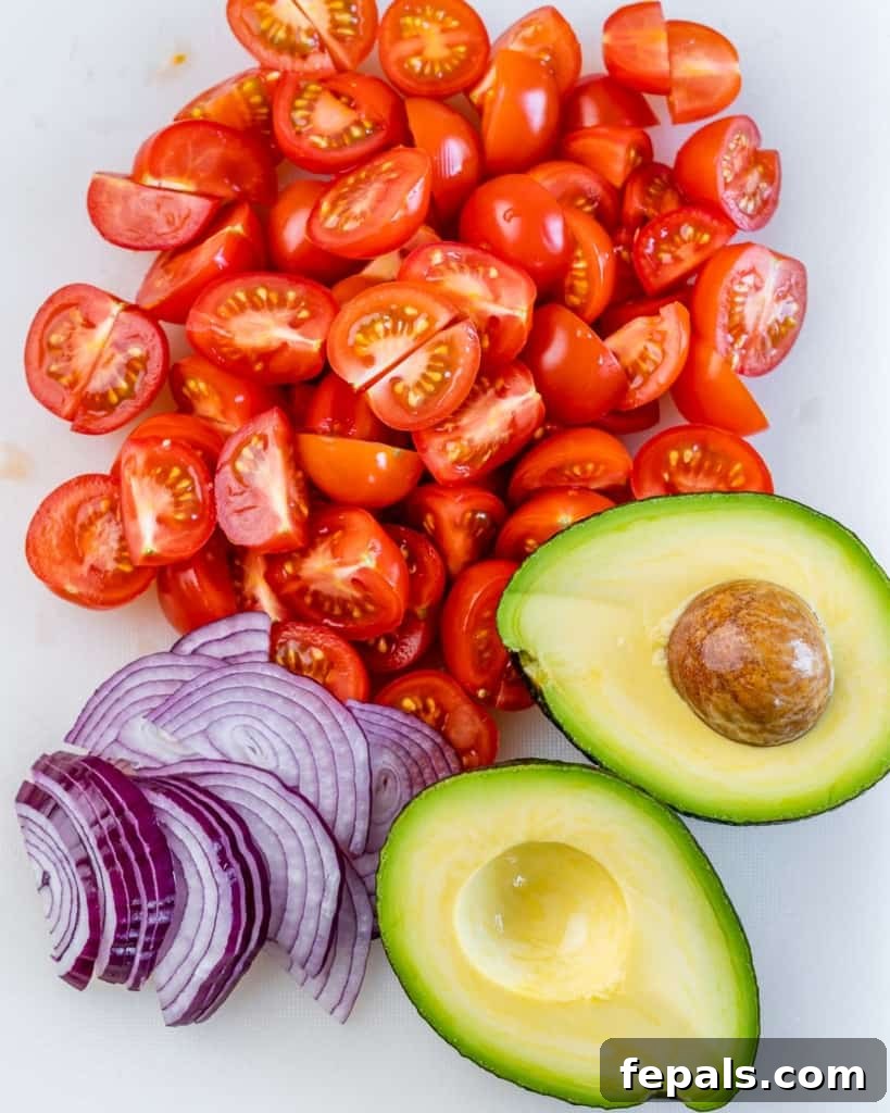Chopped cherry tomatoes, sliced red onion, and creamy avocado ready for mixing in a salad bowl.