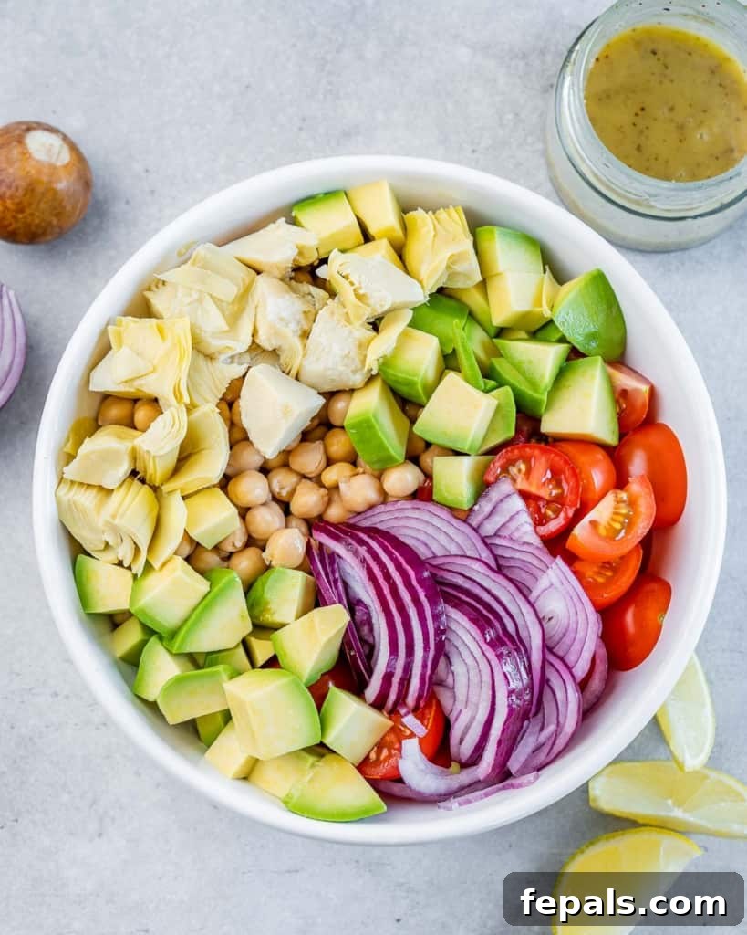 Sliced red onion, wholesome chickpeas, perfectly cubed avocado, and juicy sliced cherry tomatoes layered in a pristine white bowl, awaiting dressing.