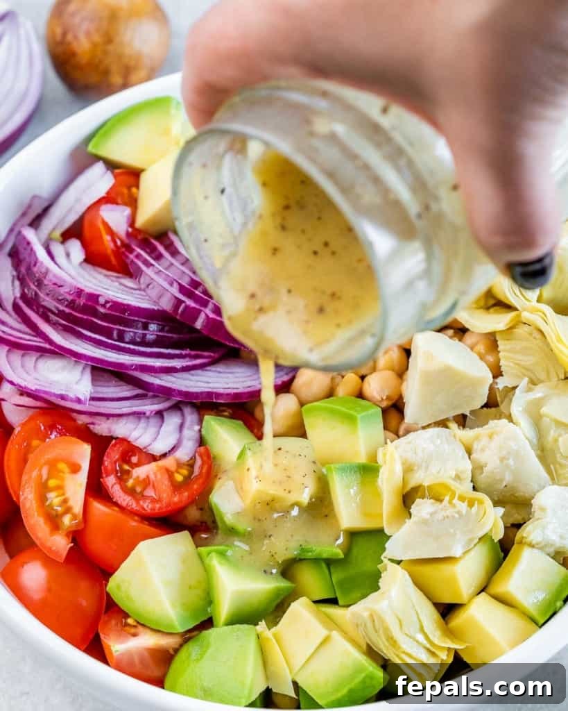 A stream of vibrant lemon-garlic dressing being poured over a fresh Mediterranean Artichoke and Tomato Salad.
