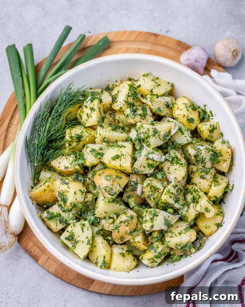Top view of herbed potato salad with vibrant green herbs in a pristine white round bowl, ready to be served.
