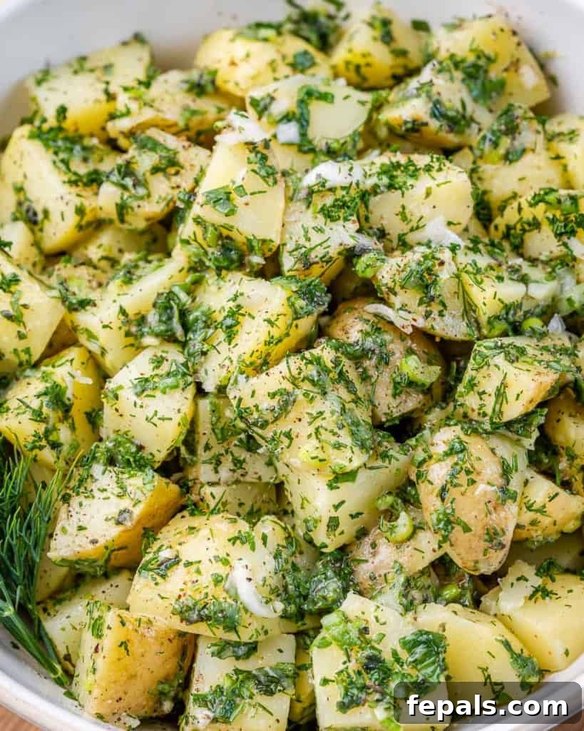 Close-up of potato salad generously coated with fresh green herbs, presented in an elegant white bowl.