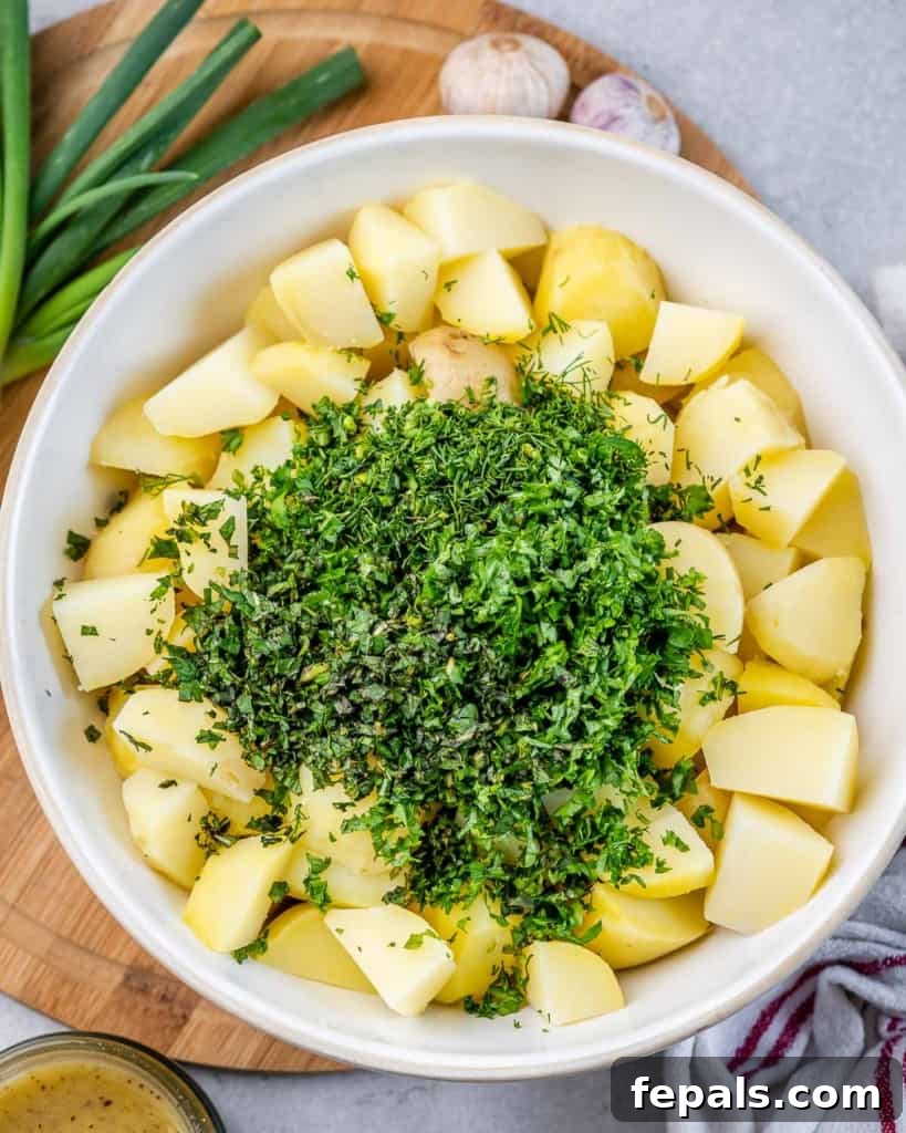Freshly chopped green herbs being added to a bowl of perfectly boiled yellow potatoes, showcasing the vibrant ingredients coming together.
