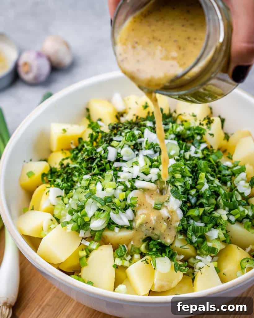 A close-up shot of a zesty vinaigrette being poured over warm, tender potatoes and a medley of chopped fresh herbs, ready for tossing.