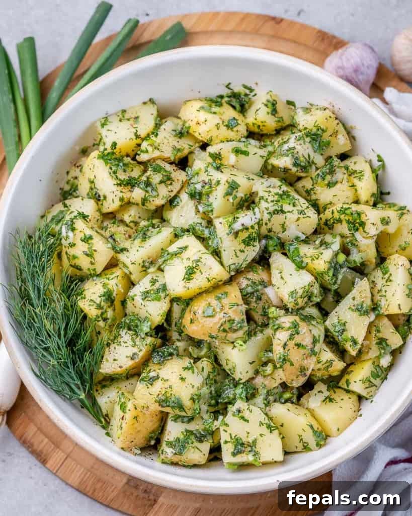 An inviting top-down view of a generously herbed green potato salad, served in a classic round white bowl, perfect for a vibrant side dish.
