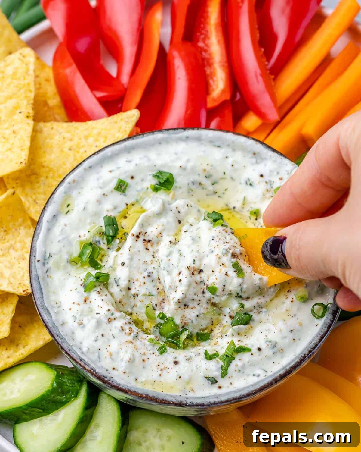 A hand dipping a vibrant red bell pepper strip into a bowl of creamy herbed cottage cheese dip, highlighting its perfect dipping consistency.
