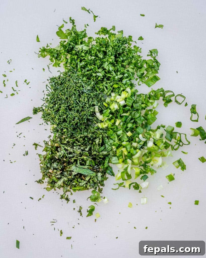 Fresh dill, mint, and parsley are meticulously minced on a clean cutting board, ready to be incorporated into the cottage cheese dip.