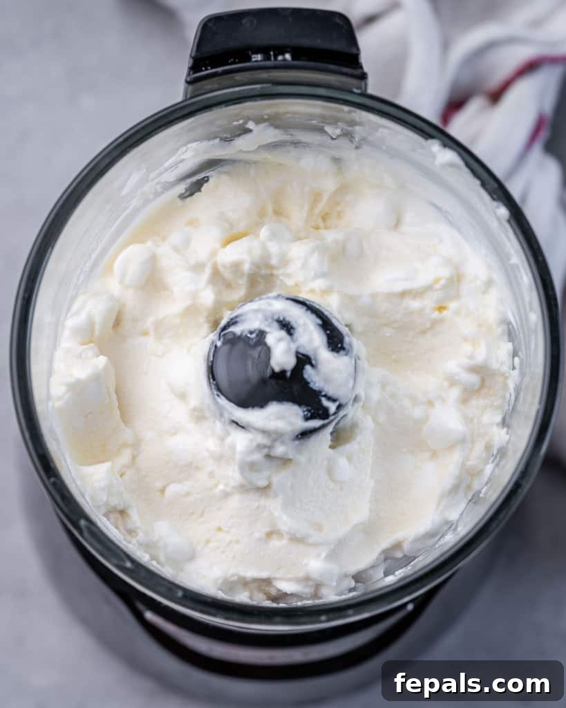 Creamy cottage cheese is being added to a food processor, poised to be blended into a smooth and delicious dip.