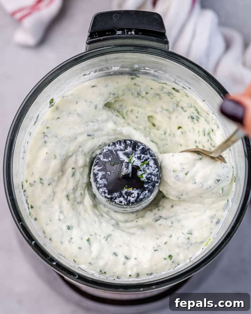 Creamy cottage cheese expertly blended with an aromatic medley of fresh herbs inside a food processor, showcasing its smooth, vibrant texture.