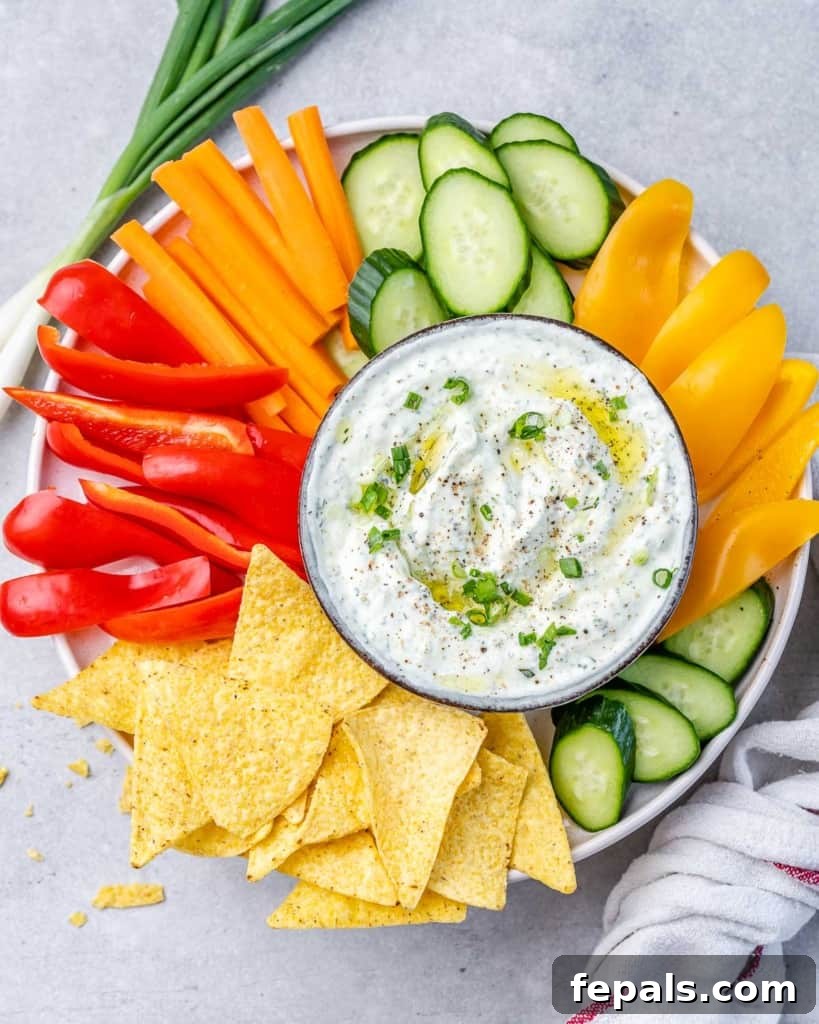 A beautifully arranged platter showcasing a bowl of creamy herbed cottage cheese dip surrounded by an abundance of colorful, freshly cut vegetables and crispy chips, perfect for a healthy snack or appetizer.