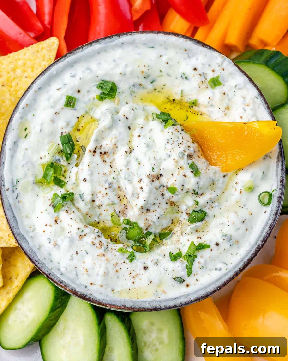 A close-up of creamy herbed cottage cheese dip in a bowl, with a bright yellow bell pepper slice perfectly dipped, showcasing the dip's rich texture and inviting color.