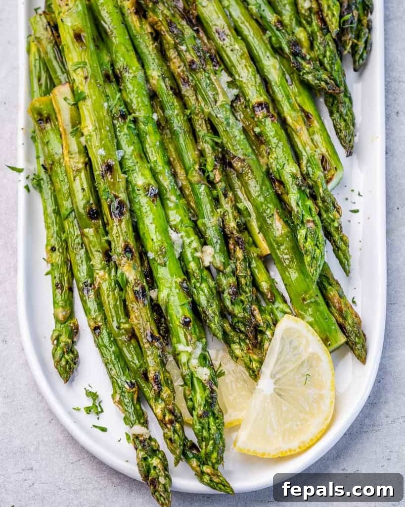 Charred Asparagus with Zesty Lemon-Garlic 2 Top view of grilled asparagus on a white plate with lemon garnish.