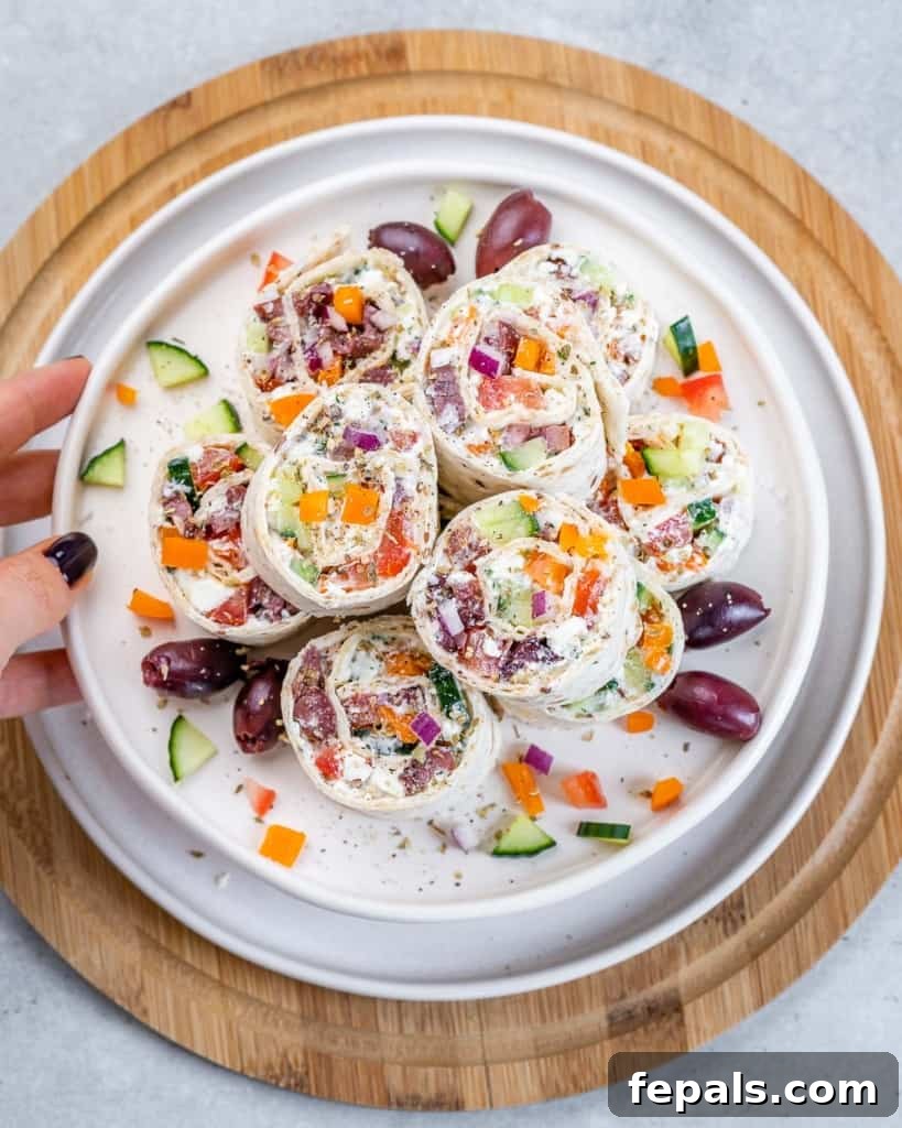 Savory Vegetable Spirals 2 Top view of colorful Greek Veggie Pinwheels arranged beautifully on a white round platter, garnished with fresh herbs.