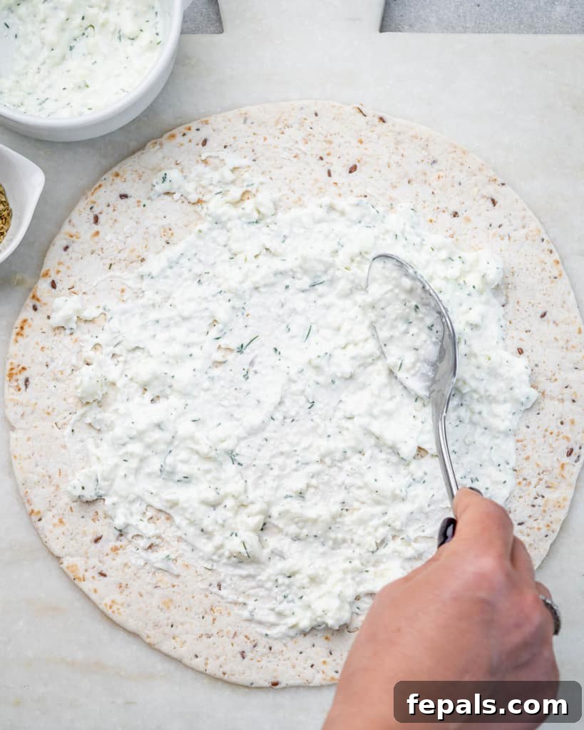 Savory Vegetable Spirals 6 A large tortilla laid flat on a surface with the creamy feta-tzatziki spread evenly applied, leaving a border.