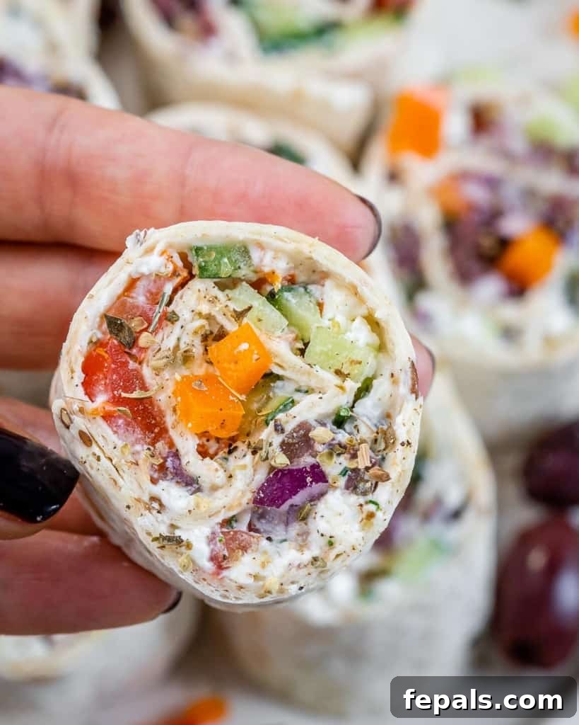 Savory Vegetable Spirals 8 A hand holding a single, perfectly sliced Veggie Pinwheel, showing the intricate layers of vegetables and spread.