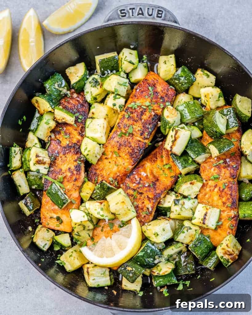 Effortless Cajun Baked Salmon 2 Top view of four seasoned salmon fillets and zucchini baking on a black skillet.