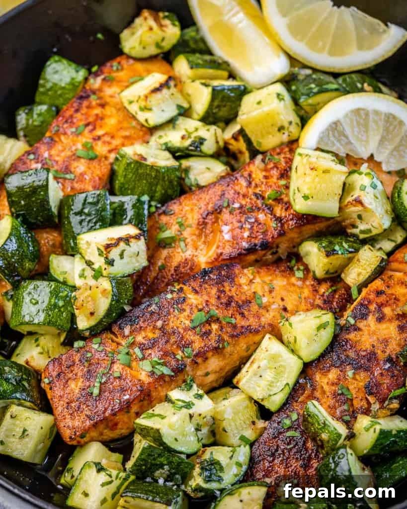 Effortless Cajun Baked Salmon 3 Close-up image of a perfectly baked salmon fillet on a black skillet with chunks of tender zucchini.