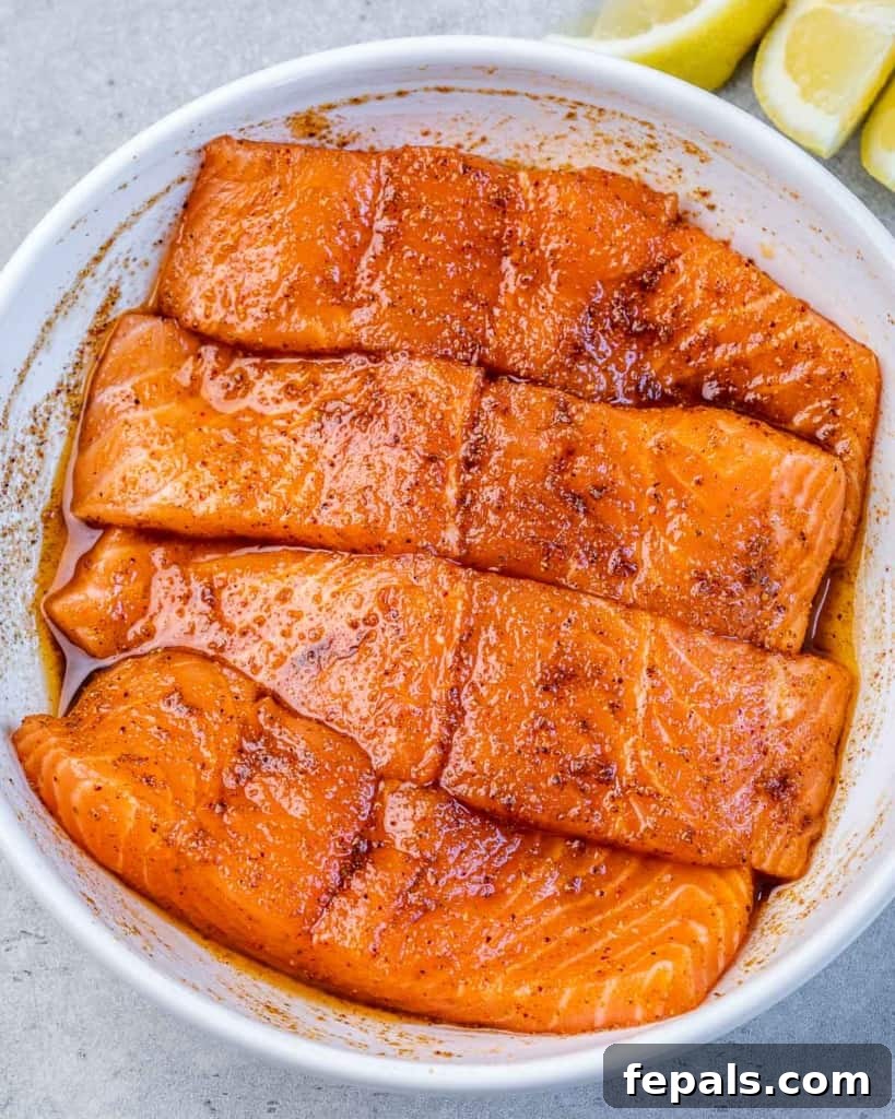 Effortless Cajun Baked Salmon 5 Four salmon fillets seasoned with Cajun spices on a round white plate, ready for cooking.