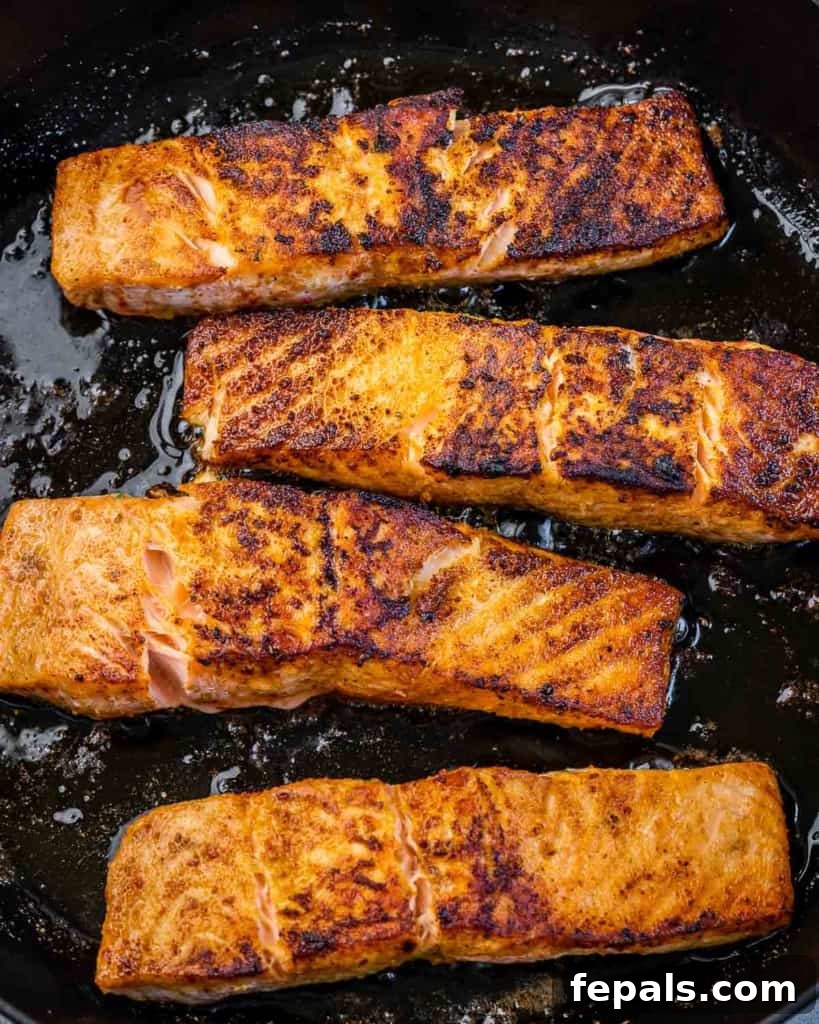 Effortless Cajun Baked Salmon 6 Four salmon fillets being sautéed in a black skillet, showing a nice sear on the underside.