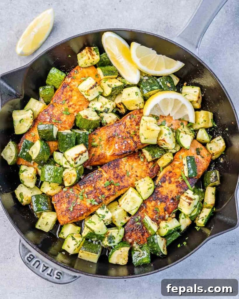 Effortless Cajun Baked Salmon 10 Top view of four baked salmon fillets with chopped zucchini on a pan, garnished with lemon slices and fresh herbs.