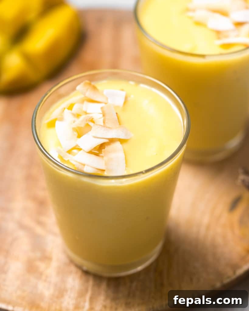 Tropical Mango Delight 10 side shot of mango smoothie in a clear cup topped with toasted shaved coconut