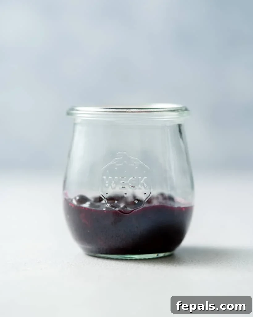 Adding blueberry sauce to the bottom of a glass jar, forming the first layer of the pudding.