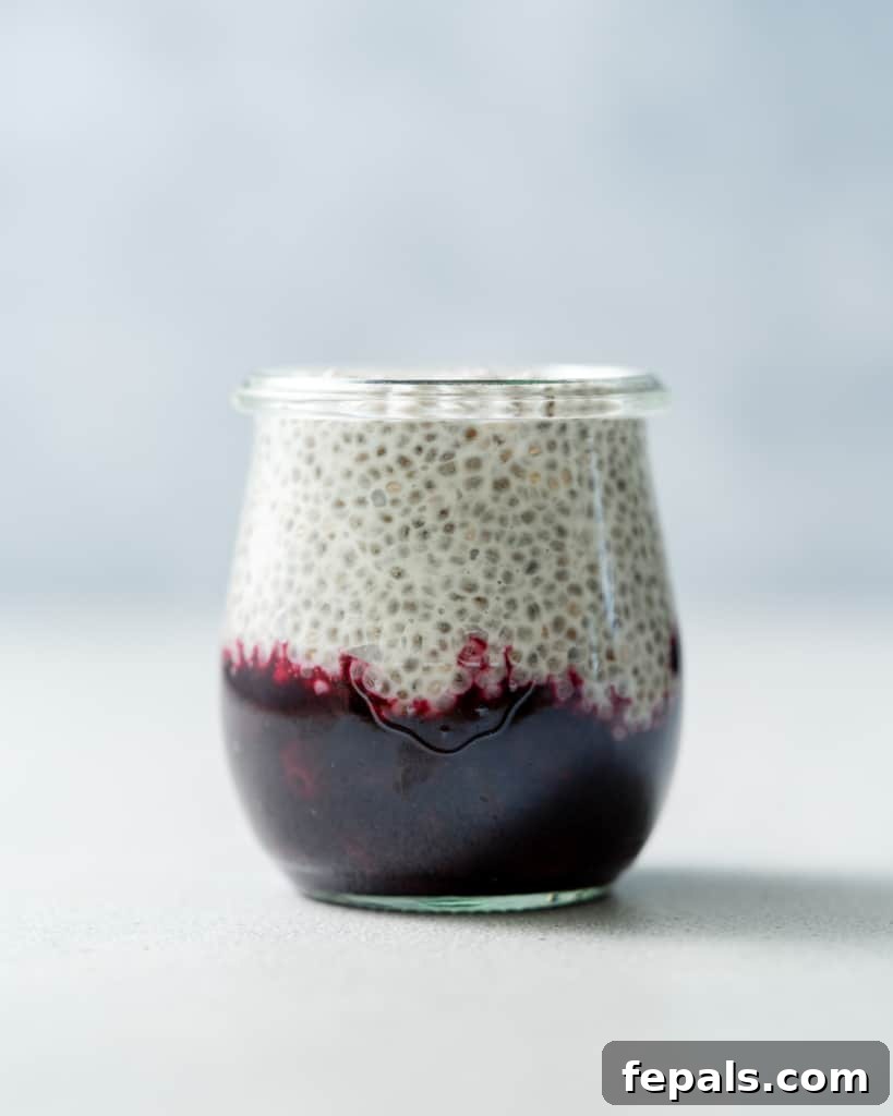 Layering chia pudding over the blueberry sauce in a glass jar, building the delicious dessert.