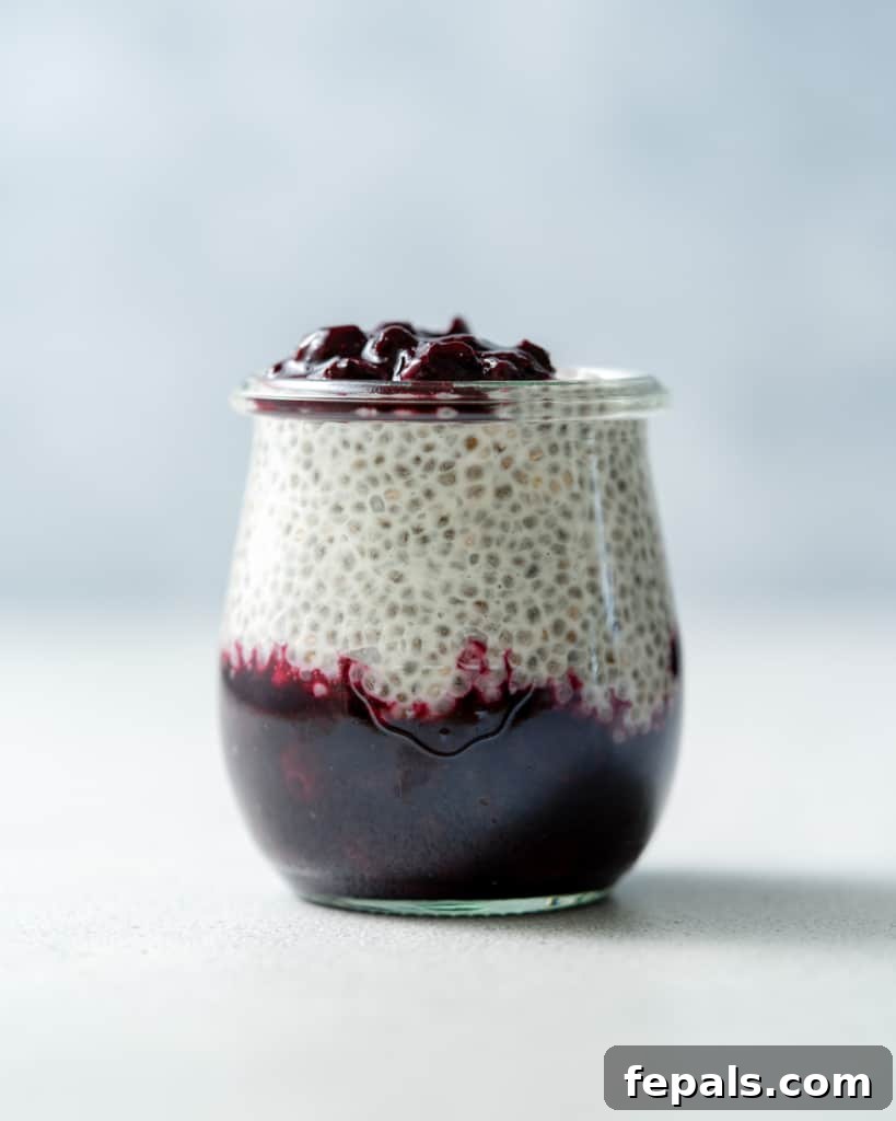 A completed glass jar with distinct layers of coconut chia pudding and blueberry sauce, ready to be enjoyed.