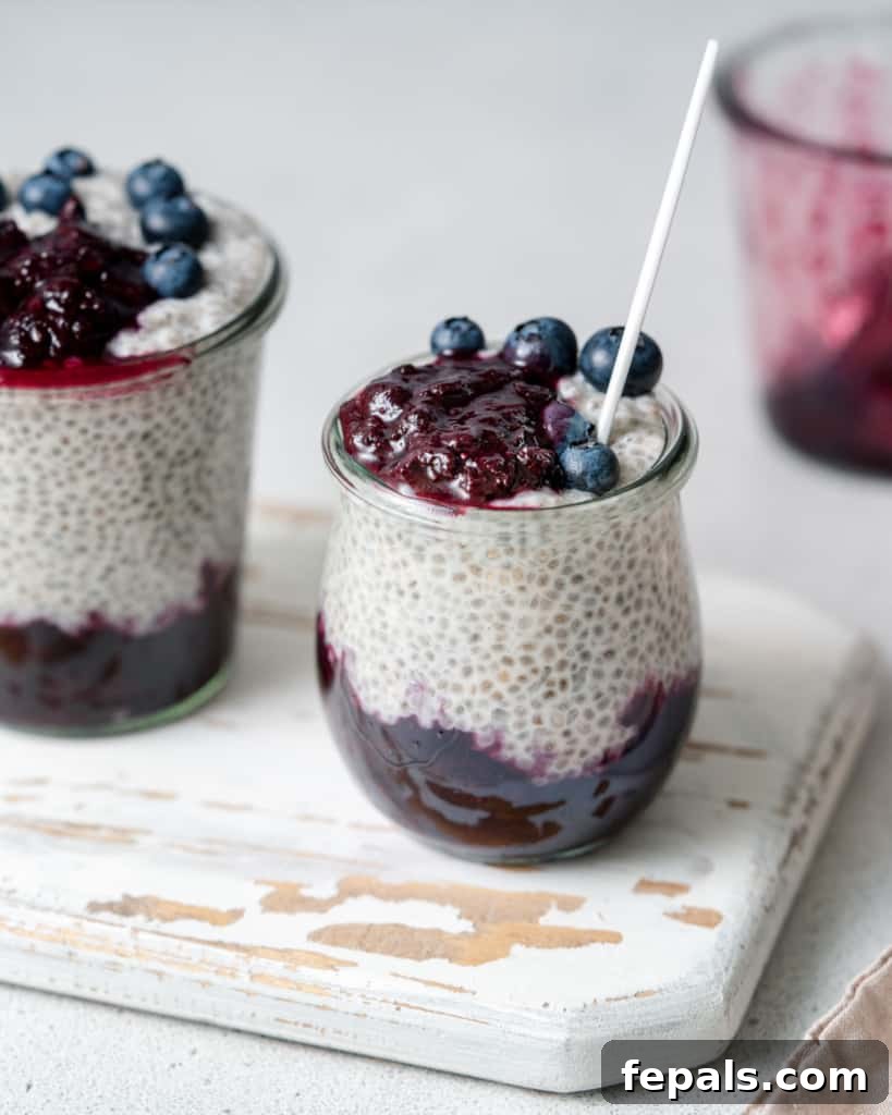 Side shot of blueberry chia pudding with a spoon in a glass jar, showing the layers of creamy pudding and fruit sauce.