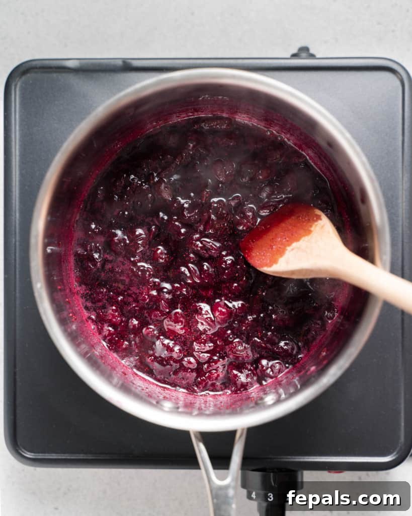 Stirring blueberries in a saucepan over heat, showing the sauce cooking process.
