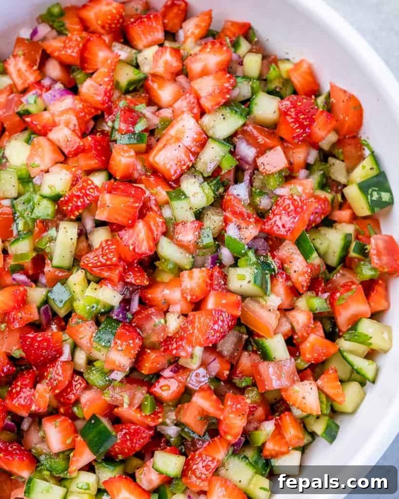 Diced strawberries, cucumbers, jalapeños and red onion in a large white bowl.