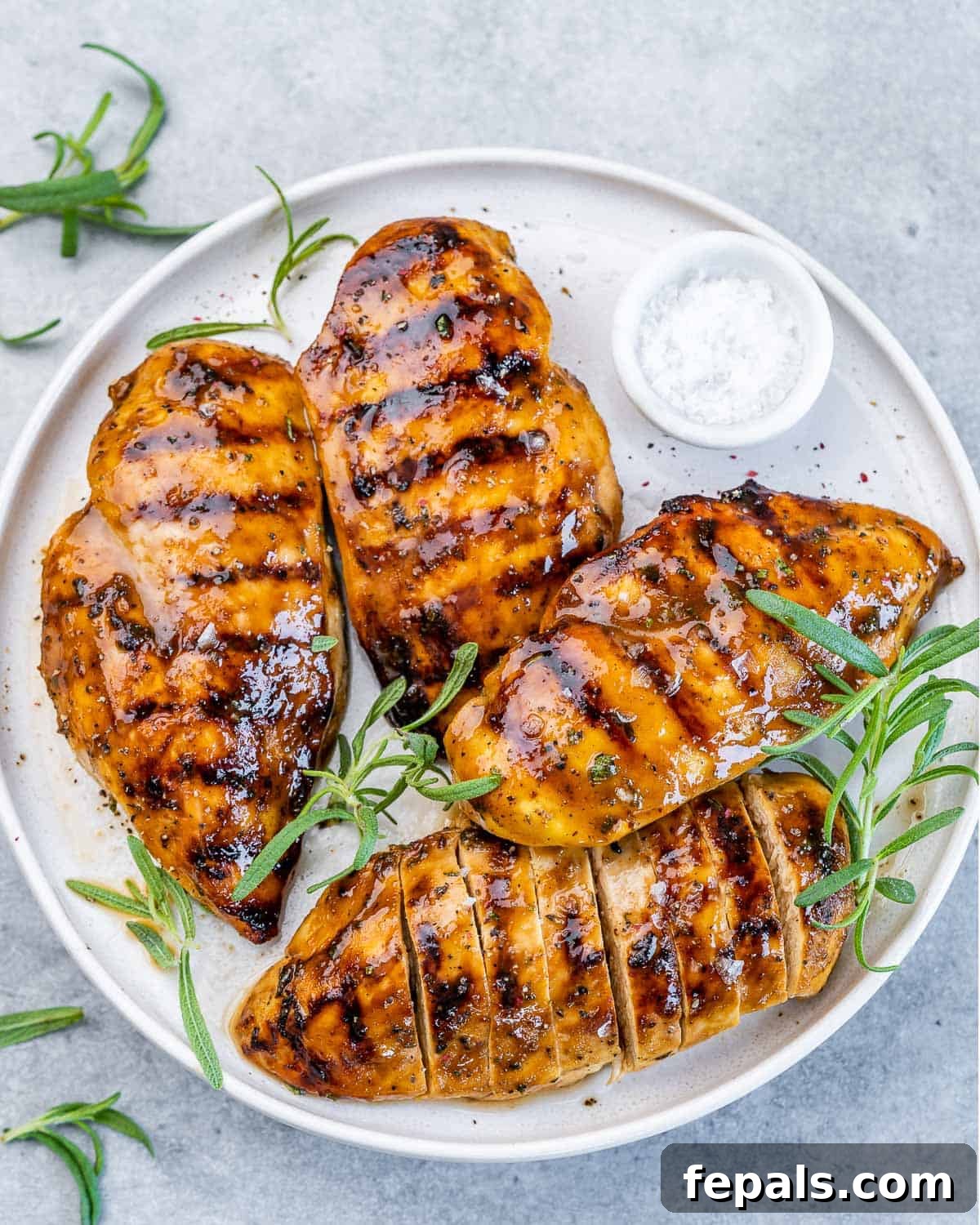 Sweet and Savory Maple Rosemary Chicken 2 Top view of 4 grilled chicken breasts over a white plate, garnished with fresh rosemary.