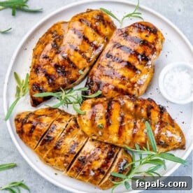 Sweet and Savory Maple Rosemary Chicken 12 Top view of 4 grilled chicken breasts over a white plate, garnished with rosemary.