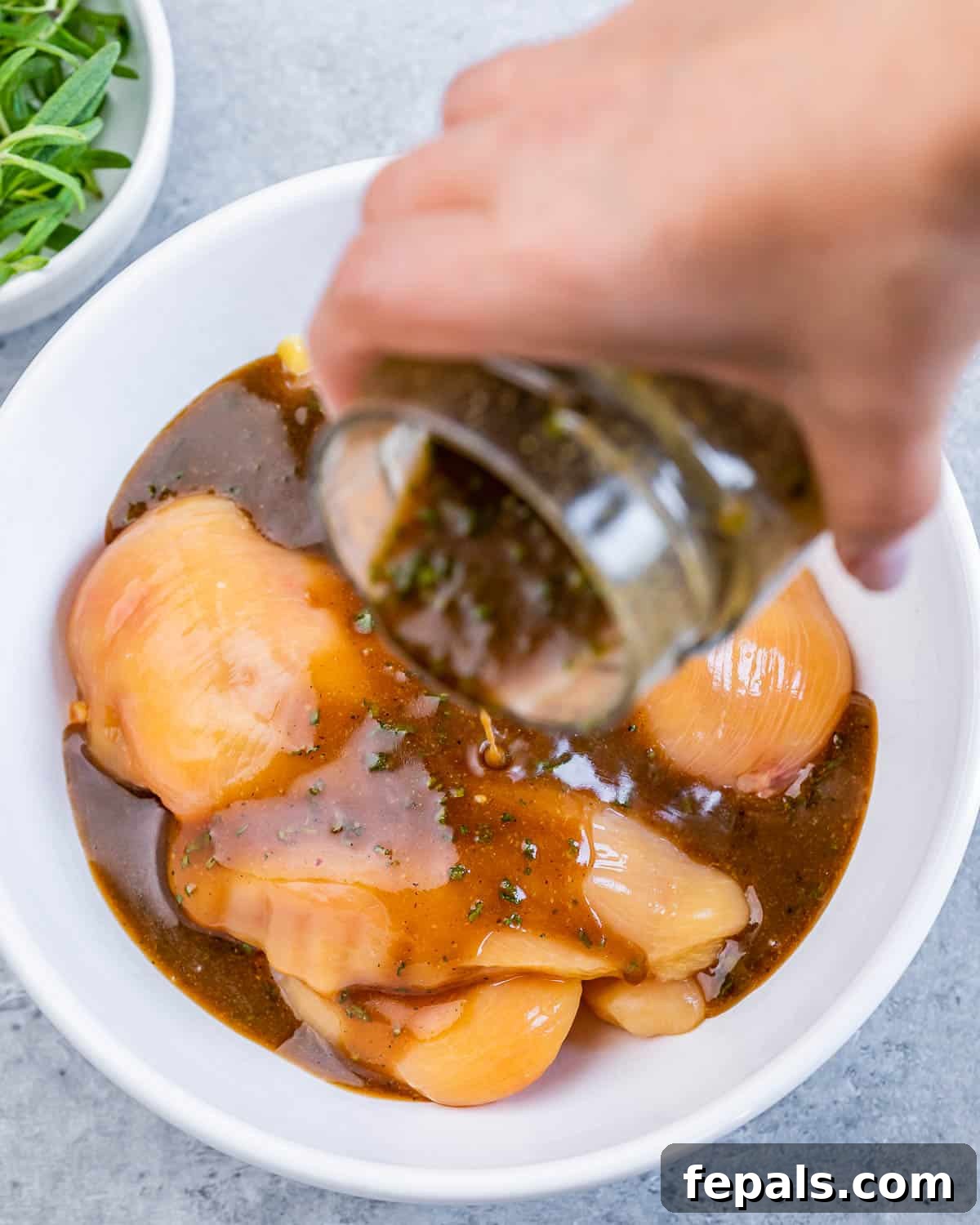 Sweet and Savory Maple Rosemary Chicken 5 Pouring homemade maple rosemary marinade over raw chicken breasts in a shallow dish.