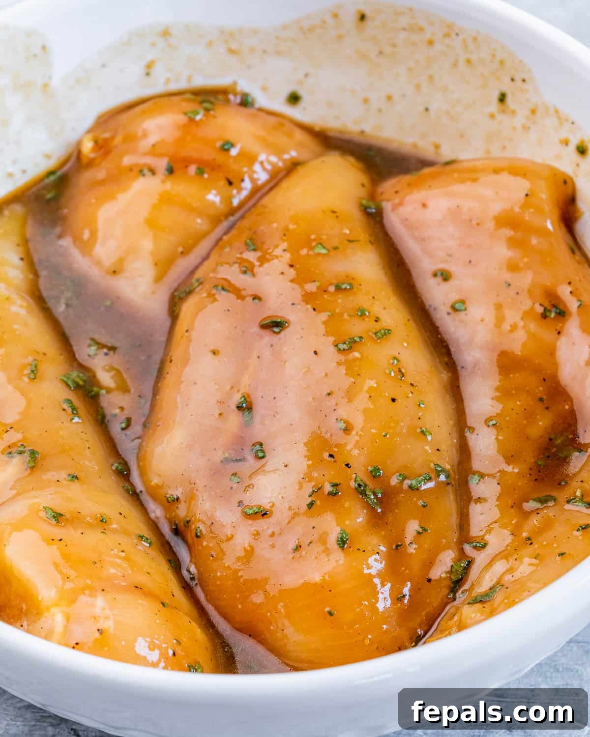 Sweet and Savory Maple Rosemary Chicken 6 Raw chicken breasts fully coated and marinating in a rich brown sauce in a dish.