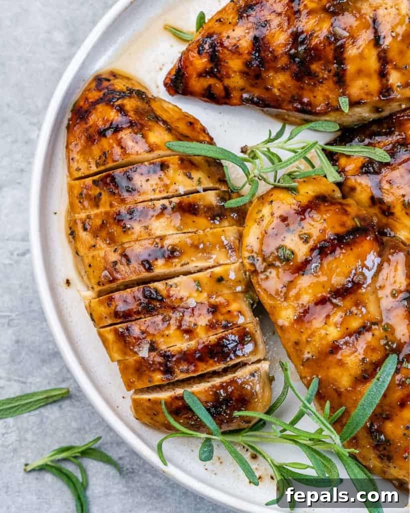Sweet and Savory Maple Rosemary Chicken 8 Sliced grilled chicken breast served on a white plate with fresh rosemary garnish and a light drizzle of sauce.