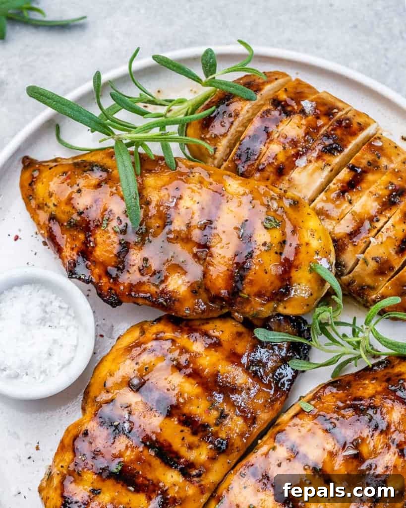 Sweet and Savory Maple Rosemary Chicken 9 Top view of 4 grilled chicken breasts on a white plate, beautifully garnished with fresh rosemary sprigs.