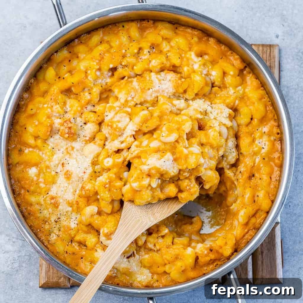 Roasted Pumpkin Mac and Cheese 11 Top view wooden spoon in pumpkin mac and cheese in pan.